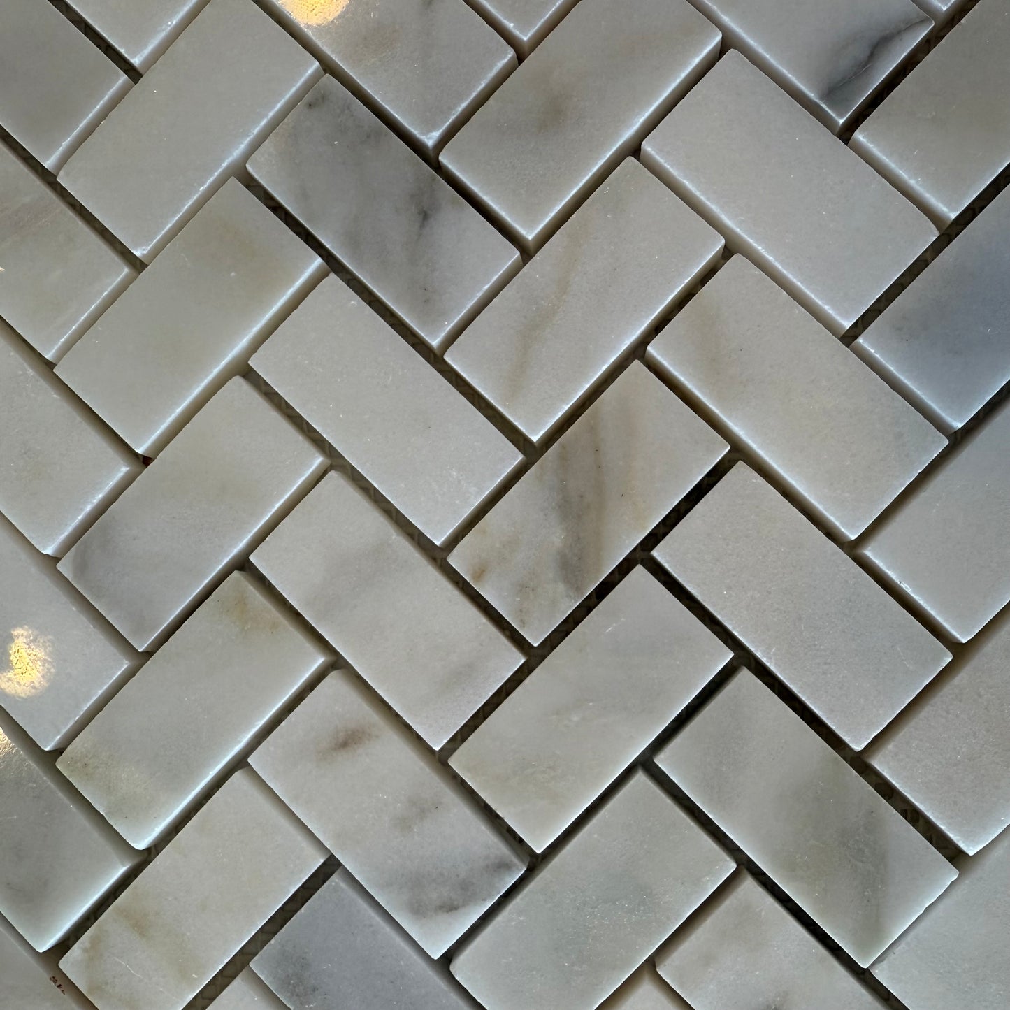 Close-up of herringbone patterned tiles with a marble-like texture.