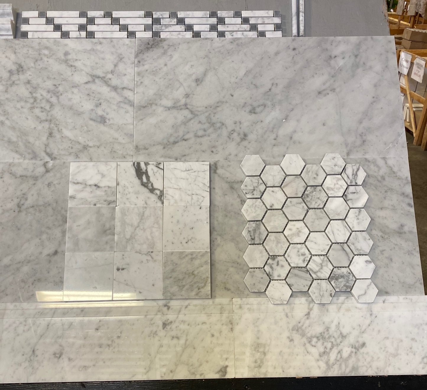 A display of marble-look tile samples, including large rectangular slabs and a hexagonal mosaic sheet, shown on a showroom floor.