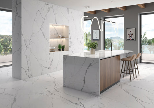 A modern kitchen island with a white and gray marble-look countertop and base, paired with light wood side panels and three bar stools, set in a bright contemporary kitchen with large windows.