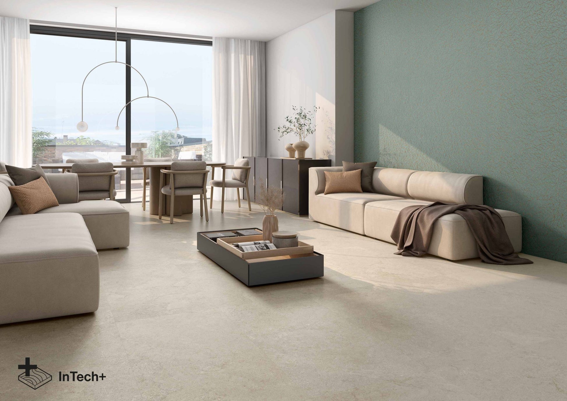 A modern living room featuring light beige textured flooring, a beige sectional sofa, a matching sofa on the right against a sage green wall, and a dark gray rectangular coffee table in the center. Large windows in the background offer a view of the sea and sky.
