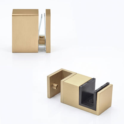 Two modern wall-mounted hardware pieces in a brushed brass/gold finish, shown on a clean white studio background. One piece is positioned upper left and the other lower right, both displaying a square block design with a side screw and a dark inner insert.