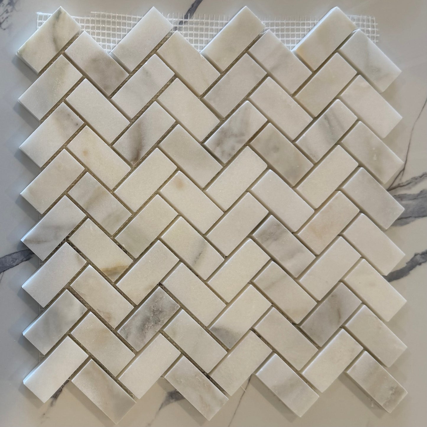 Marble mosaic tile sample with herringbone pattern on a white background