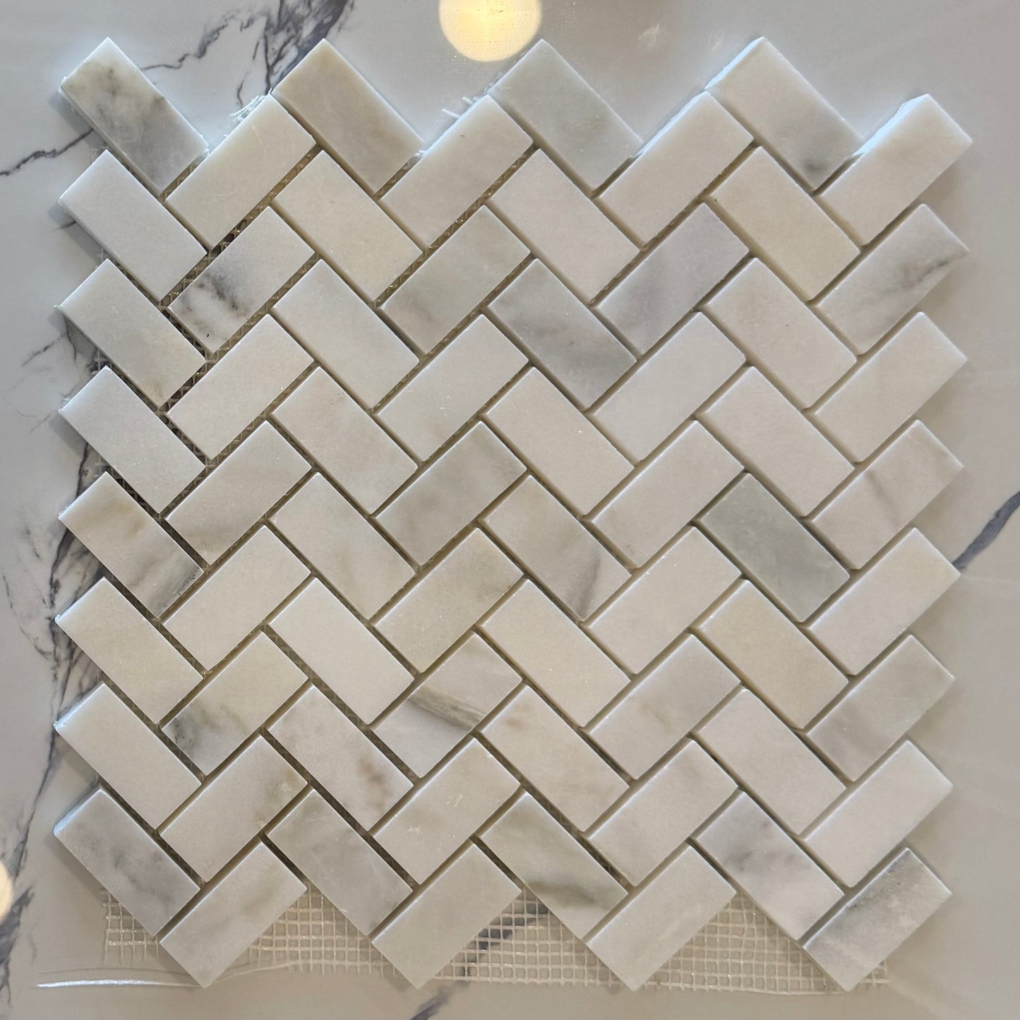 Marble mosaic tile sample with herringbone pattern on a marble surface