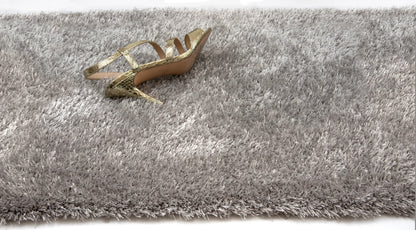 A single gold strappy high-heeled shoe placed on a thick, shaggy gray rug against a white background.