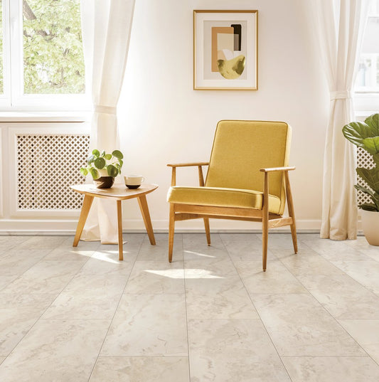 A room with light beige travertine tiles on the floor, featuring a yellow armchair, a wooden side table with a plant, and a framed picture on the wall.