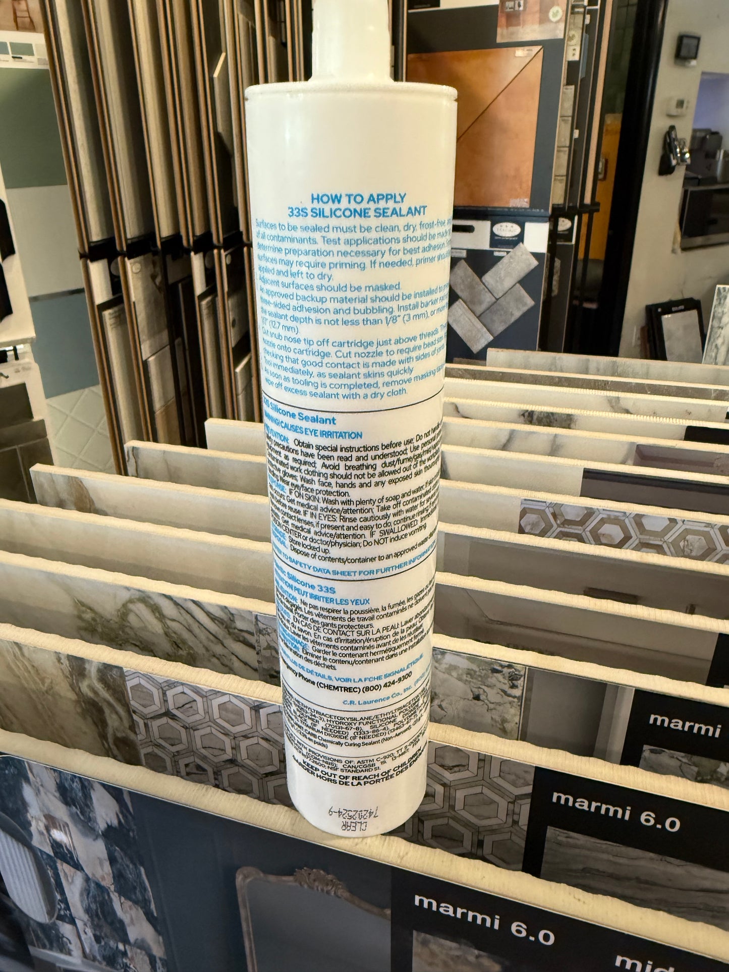 Tube of silicone with text and graphics on a rack with tile samples in the background