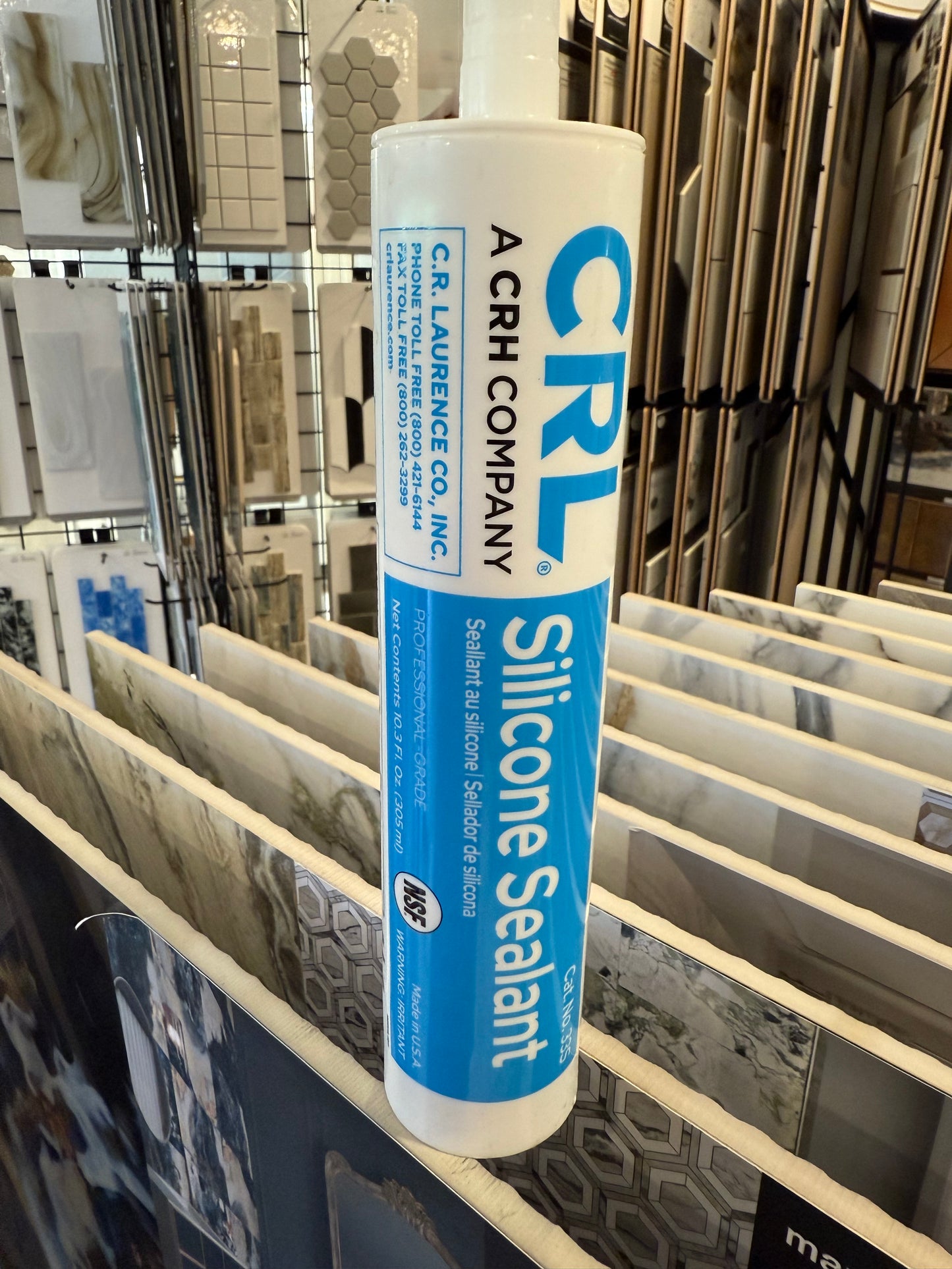 Tube of silicone with text and graphics on a rack with tile samples in the background