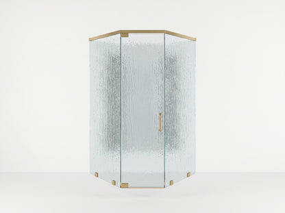 A modern hexagonal corner shower enclosure with textured, frosted glass panels and polished brass hardware, set against a clean white studio background.