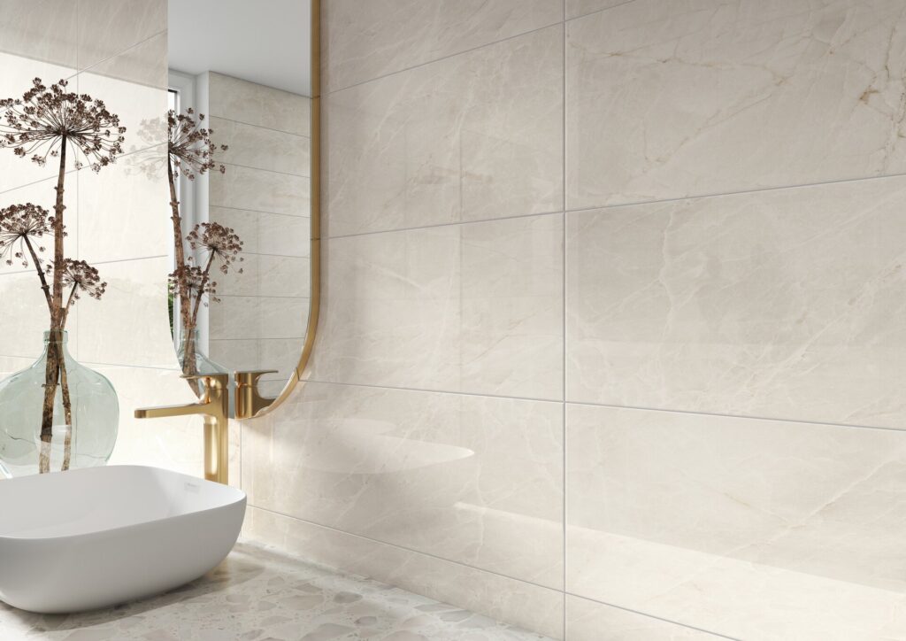 Beige marble-look wall tiles in a modern bathroom setting, featuring a white vessel sink, a gold faucet, and a gold-framed mirror.