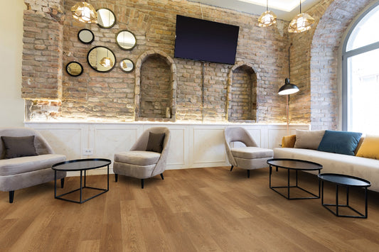 A modern living room or lounge area with light oak wood flooring, a stone brick accent wall with built-in niches and mirrors, gray armchairs, a cream sofa with blue and yellow pillows, black metal coffee tables, pendant lights, and a wall-mounted TV.
