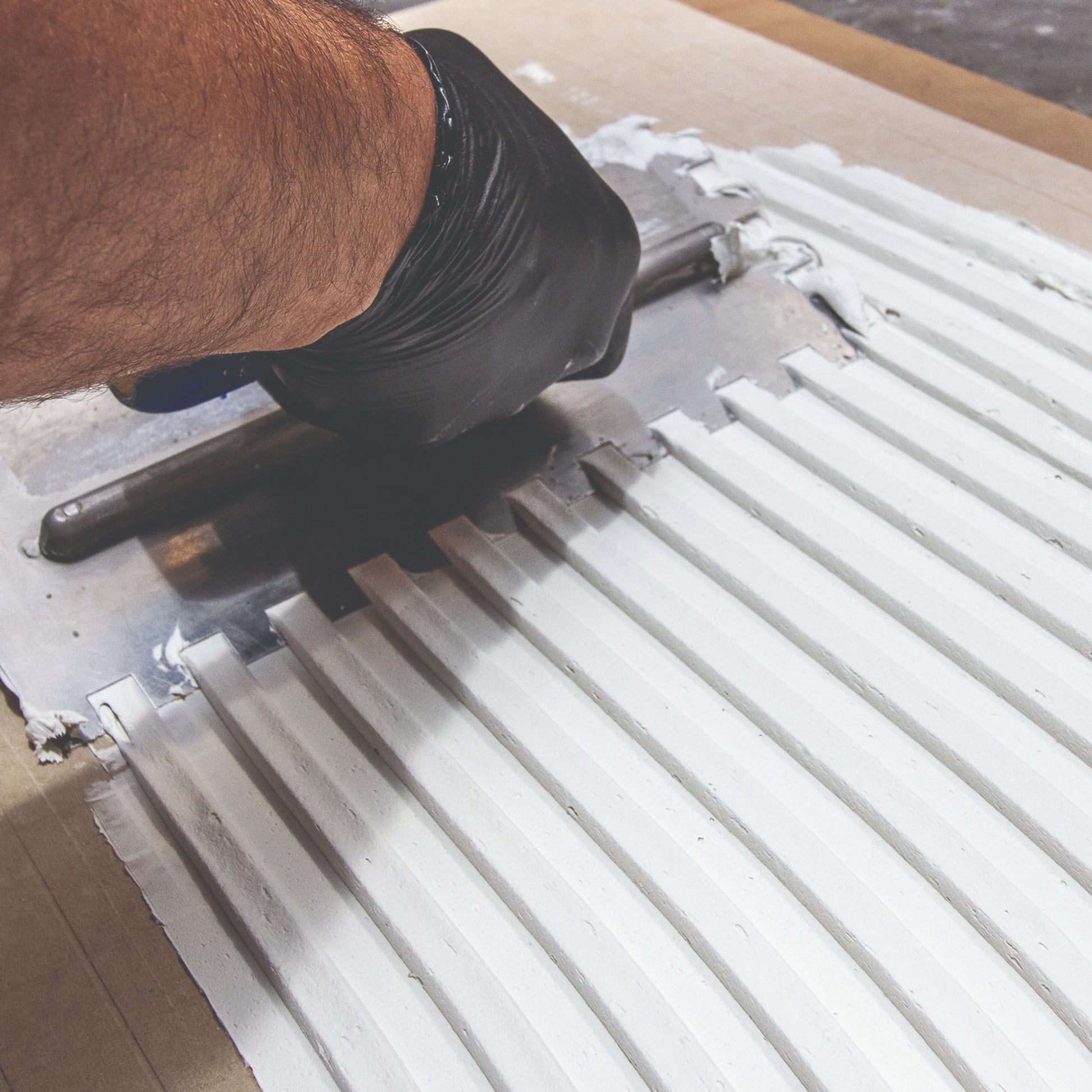 Person using a trowel to spread creamy thinset adhesive on a piece of James Hardie board