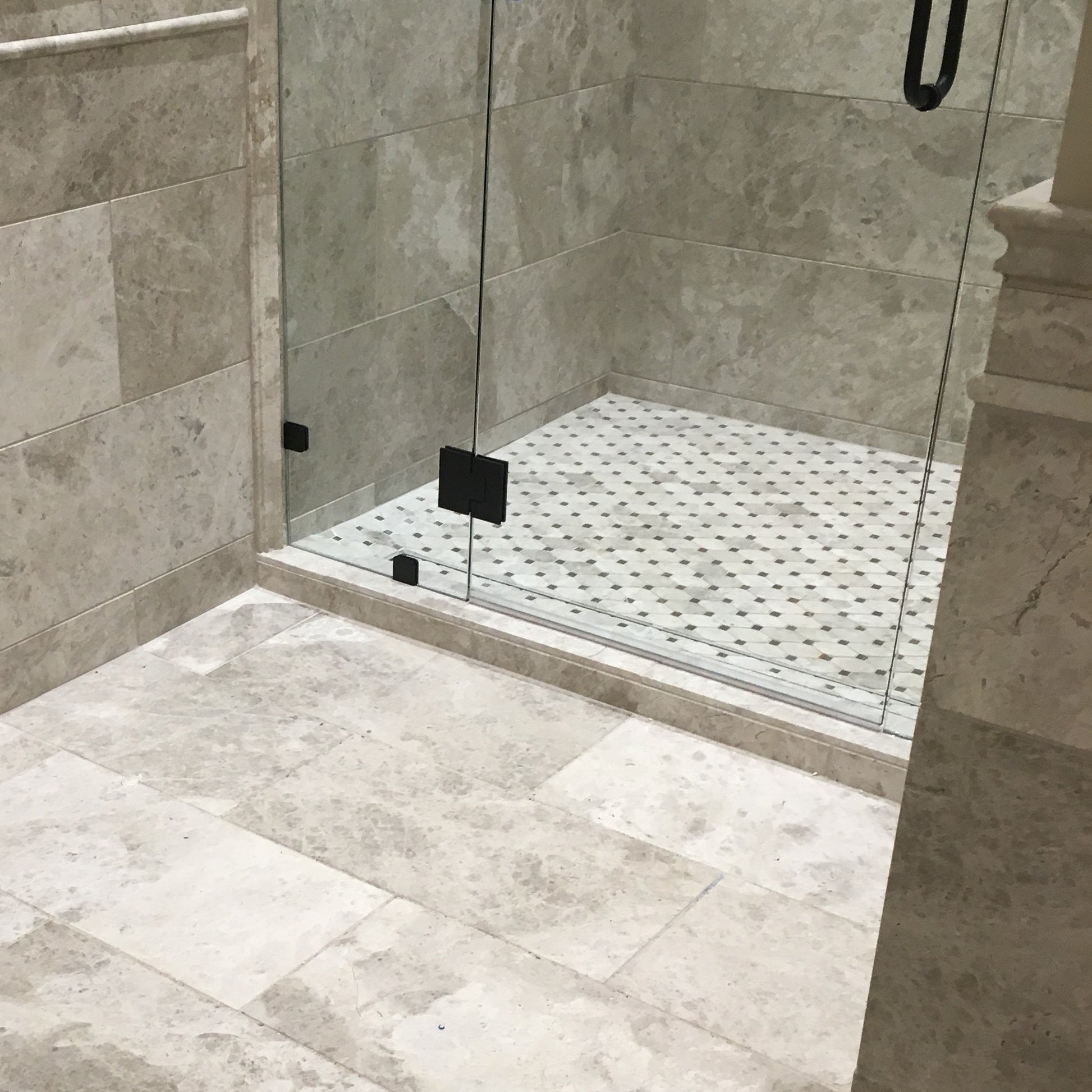 Close-up of a tiled bathroom floor with a glass shower enclosure.