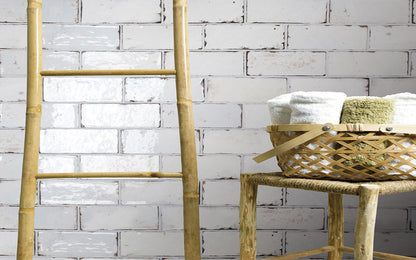 A natural bamboo ladder leans against a distressed white brick wall next to a woven rattan stool holding a basket of folded white towels.