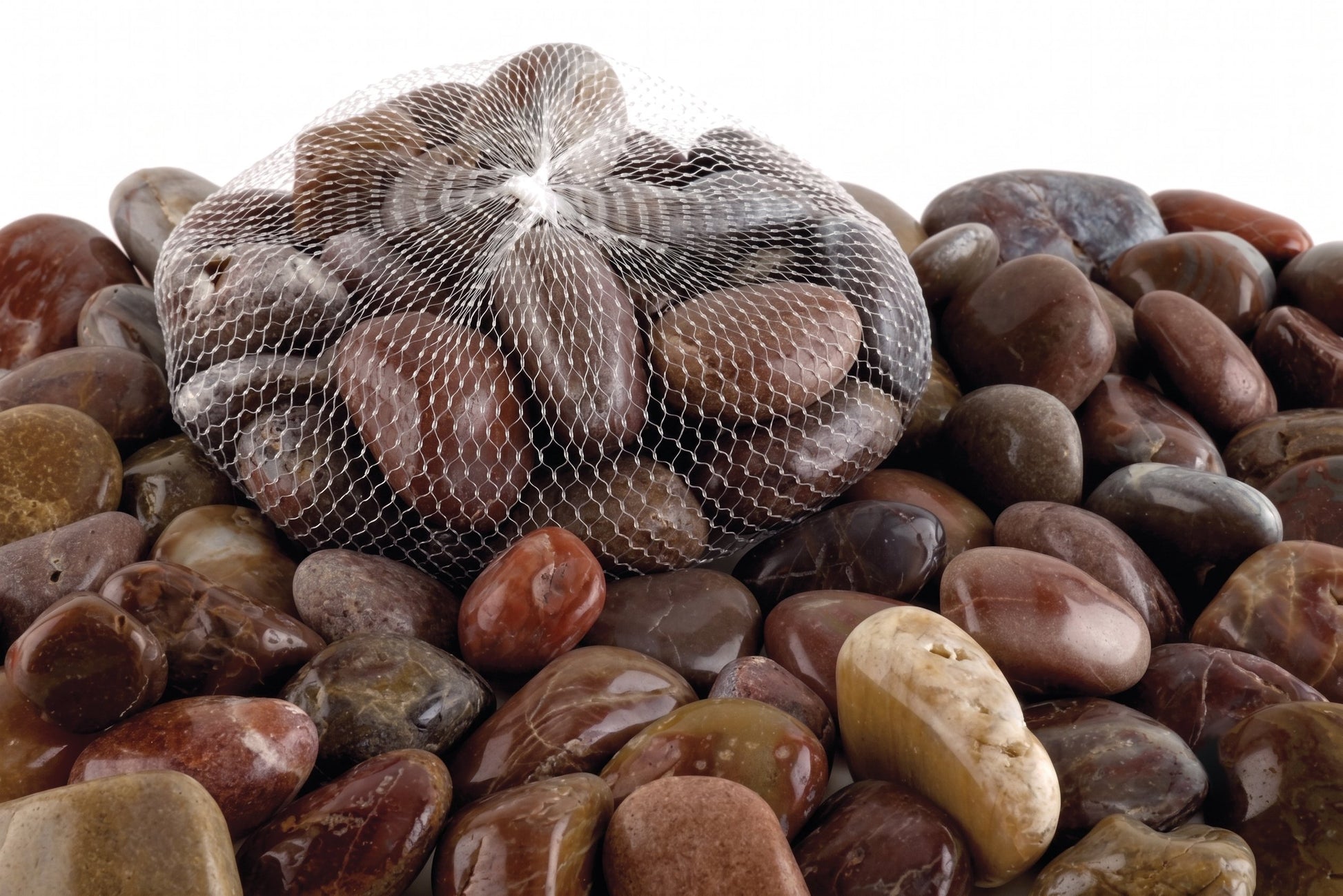 A mesh bag filled with smooth decorative pebbles and river stones, placed on top of a larger pile of similar stones against a white background.
