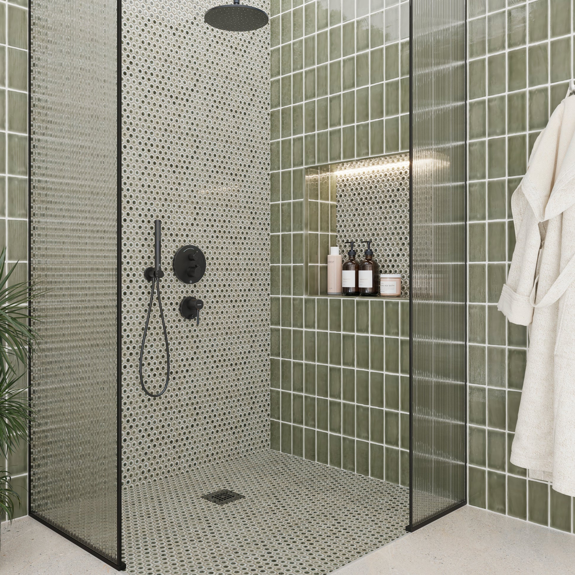 Modern shower with green tiled walls and a white bathrobe.
