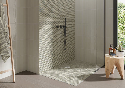 Modern shower with mosaic tile wall and wooden stool with bottles and plant