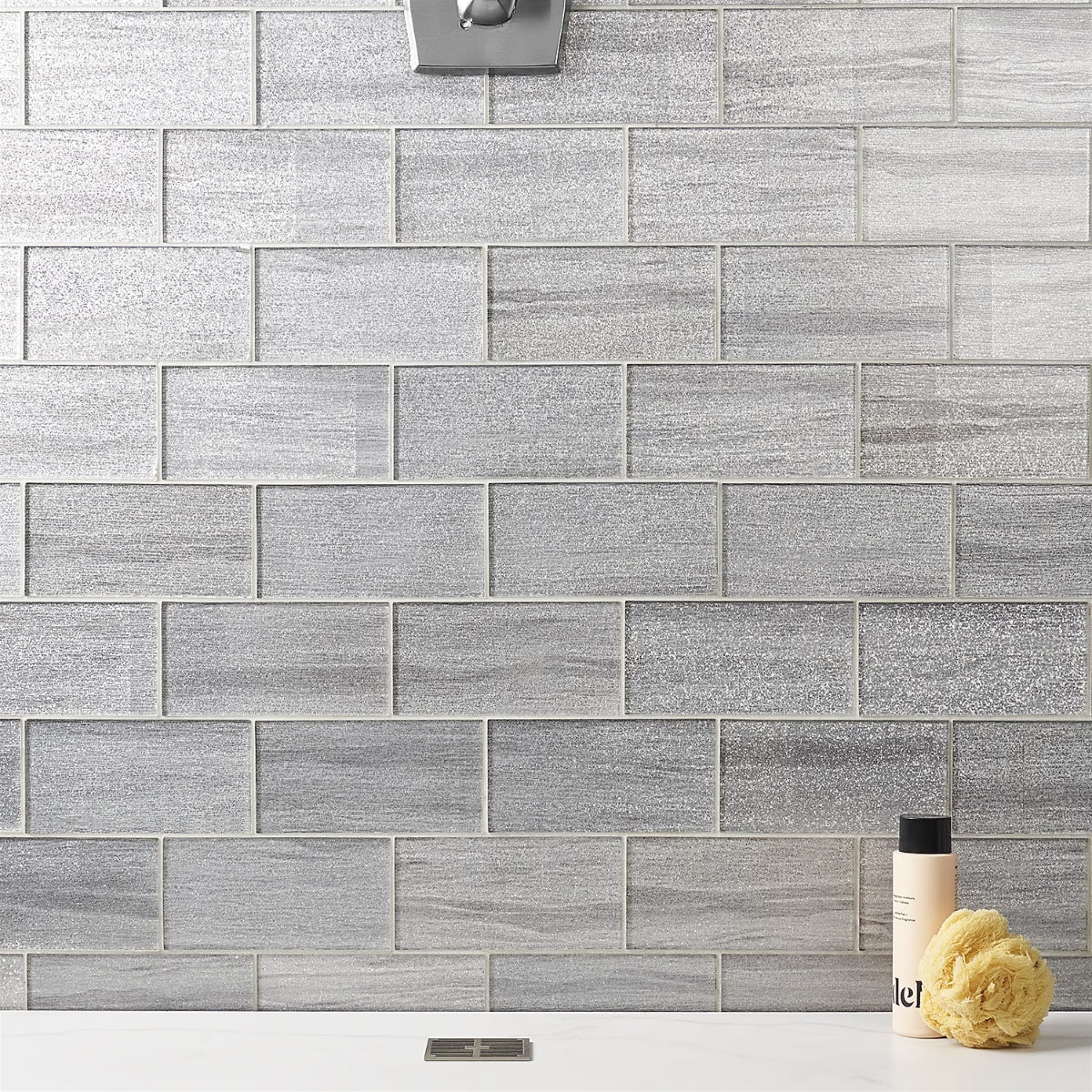 Gray tiled wall with a bottle and sponge on a white surface