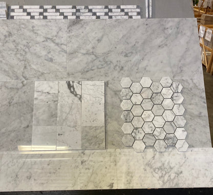 A display of marble-look tile samples, including large rectangular slabs and a hexagonal mosaic sheet, shown on a showroom floor.
