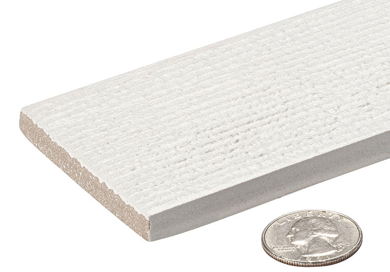 A close-up of a white textured rectangular tile or board with a coin placed in front for scale, on a plain white background.