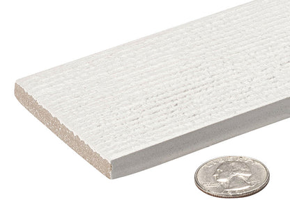 A close-up of a white textured rectangular tile or board with a coin placed in front for scale, on a plain white background.